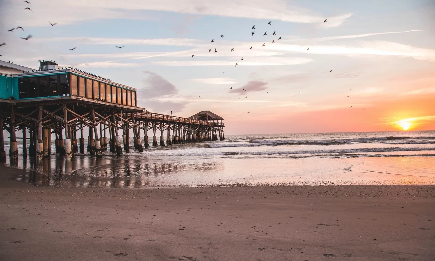 A pier with birds flying over it at sunset.